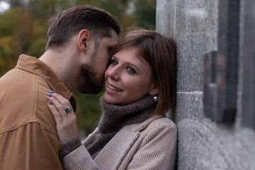 Young man kissing young woman outside. She hugs him by the shoulders and smiles