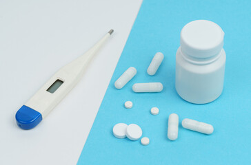 On a white and blue background there is a thermometer, pills, capsules and a white container.