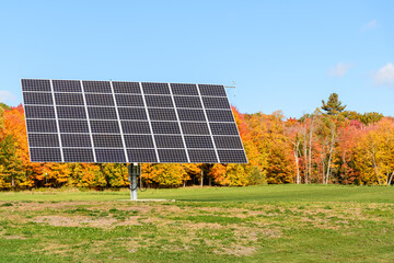Tracking solar panels in a field surrounded by a deciduous forest at the peak of fall foliage on a...