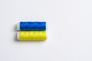 Two spools of thread for sewing are stacked in the form of the flag of Ukraine on a white background. Concept of Ukrainian patriotism and the country's garment industry. There is a free empty space.