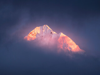 las pink sun lights on snow peaks Tomserkie through clouds in Nepal