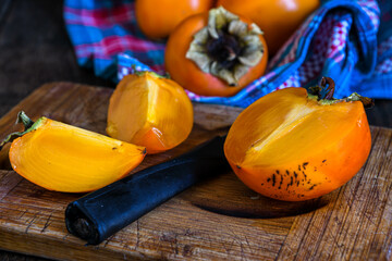 Ripe persimmon sliced on a kitchen board, a kitchen napkin and orange persimmon fruits lie on a...