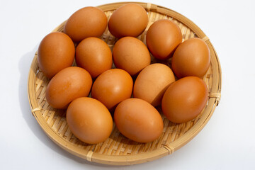 Chicken eggs in round bamboo basket on white.