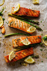 Baked salmon and green asparagus with aromatic herbs and lemon slices on baking paper top view - 468854824