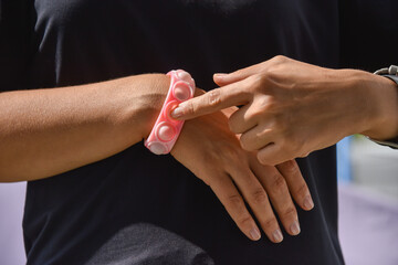 Close-up of a popit and simple dimple toy. A bracelet on a woman's hand in the form of a pink silicone anti-stress toy for children