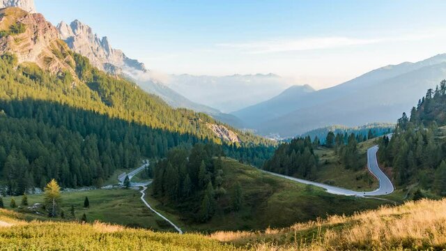 Mountain lanscape with a winding road leading down to a forested valley in the Dolomites in autumn - Time lapse