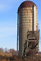 Old Grain Silo behind Dilapidated Corn Crib against Blue Sky