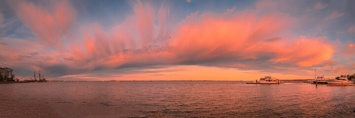 Fototapeta na wymiar Panoramic arching pink cloudscape over the Plymouth Harbor. Twilight seascape at the marina in the Atlantic ocean.