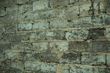 The texture of the masonry of the wall of the building is made of rough gray stone. Ancient urban architecture. Mossy, damp stones.