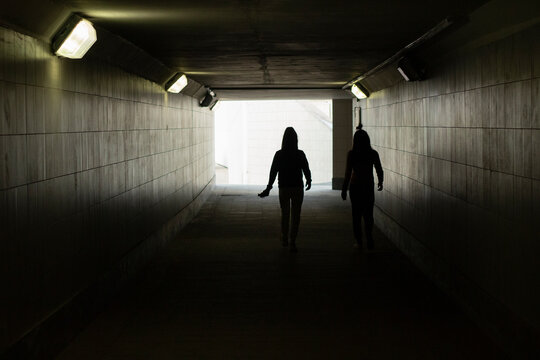 Silhouette of people in the tunnel. The girls walk through an underground tunnel.