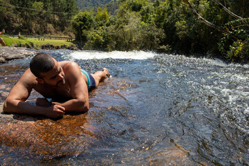 man lying on rock looking at water in waterfall in sunny day with blue sky, space for text