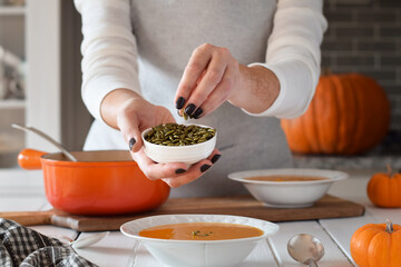 Woman garnishing squash soup with pumpkin seeds