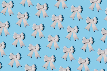 Sparkly silver bow ribbon pattern on pastel blue background. Christmas and New Year decoration idea. Minimal winter holidays concept. Flat lay, top view.