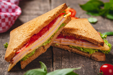 Sandwich with ham, cheese, tomatoes and lettuce leaves on wooden rustic table. Close up