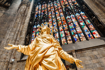 Statue of Madonna in gold against the background of a stained glass window in the Duomo. Milan,...