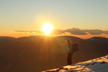 Fototapeta na wymiar young caucasian female hiker on a mountain summit at sunset - golden hour in snowy landscape