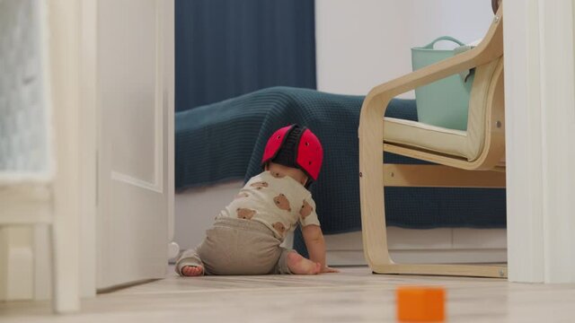 Baby wearing soft safety helmet crawling on the floor, head protector helps reduce impact of falls on hard surfaces, 7 month old caucasian toddler exploring all around the house. 4k footage