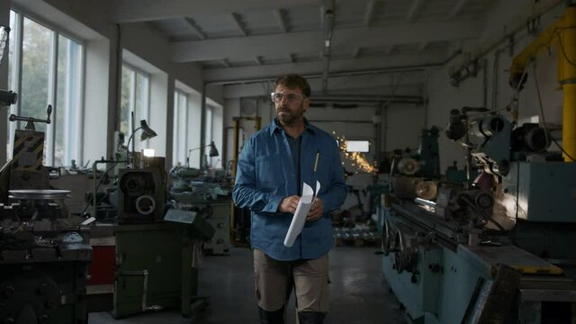 Mature industrial man working indoors in metal workshop, looking at camera.