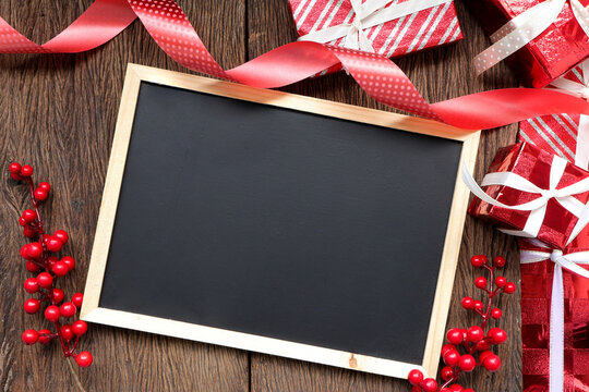 Red luxury gift box and decorations around chalkboard. Christmastime celebration. Space for text.
