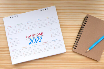 2022 Calendar, 12 months desk calendar, notebook and pencil on wooden table. Happy New year 2022 concept.