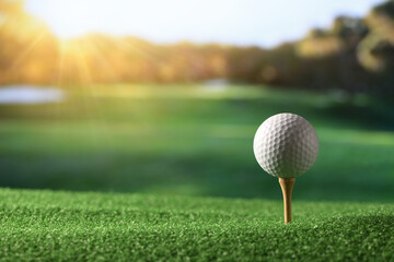 Close-up golf ball on tee with fairway golf course and morning light background.