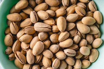 Top view close up on fresh salted roasted pistachios snack nuts in bowl with copy space on concrete table background