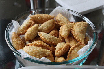 Freshly made Ghughra (Gujarati Indian crispy fried snack food with sweet, dry filling) in a glass container for Diwali