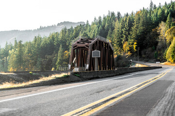 Landscape with narrow truss railway bridge next to highway road with autumn yellow trees on rocks in Columbia River Gorge