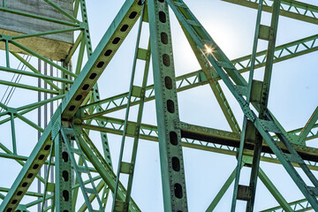 Sun glare on the intertwining openwork riveted trusses of a metal lifting bridge with a...