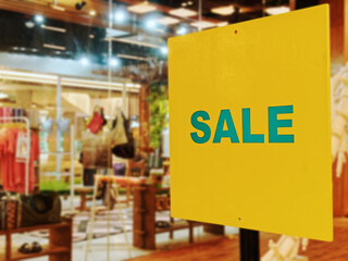 Sale Promotional Text on Yellow Label Against Blurred Clothing Store Background