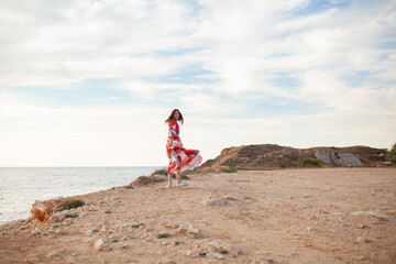 Beautiful woman in a long red dress near sea, a walk by the shore