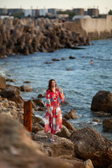 Beautiful woman in a long red dress near breakwater, a walk by the sea
