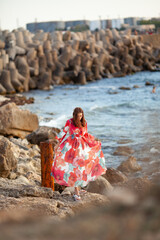 Beautiful woman in a long red dress near breakwater, a walk by the sea