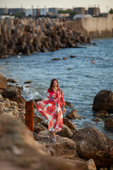 Beautiful woman in a long red dress near breakwater, a walk by the sea