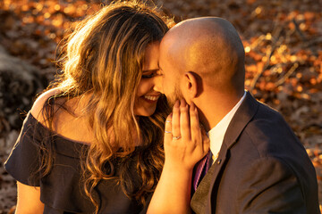 Fototapeta premium Romantic photo of a well dressed mixed race couple hugging and holding kissing each other at sunset in a city park