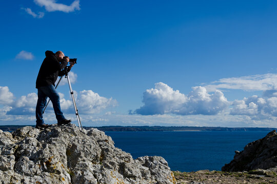 Professional nature photographer standing on a rock and taking photos of the breathtaking landscape of Brittany