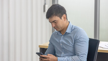 An attractive male office worker is using a smartphone to check his business and market information online. Business man use digital device to enhance his marketing. A man is chatting with his friends