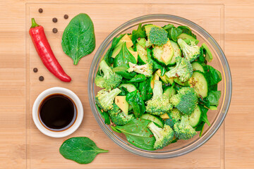 Fresh Green Salad of Avocado, Broccoli, Spinach and Cucumber with Soy Sauce and Red Hot Pepper on Wooden Cutting Board. Vegan Salad. Vegetarian Culture. Raw Food. Healthy Eating and Vegetable Diet