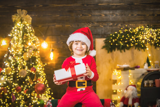Portrait of funny kid with gift looking at camera. Kid having fun near Christmas tree indoors.