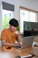 Young man drinking hot coffee and surfing internet with laptop computer at home.