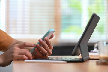Cropped shot man sitting in front of computer tablet and using mobile phone.