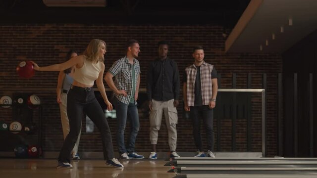 A young blonde woman makes the final throw with a bowling ball and wins the game with the support and joy of her friends of different nationalities. Rejoice and celebrate the victory