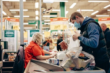 Man in protective medical mask buying food at grocery store or supermarket during quarantine, lockdown, coronavirus pandemic.