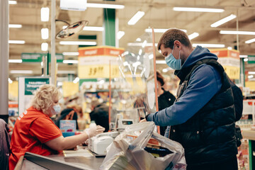 Obraz premium Man in protective medical mask buying food at grocery store or supermarket during quarantine, lockdown, coronavirus pandemic.