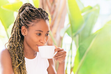 An African American woman drinking a cup of coffee while looking down outside