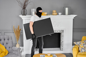 Thief with black balaclava stealing modern expensive television. Masked face. Man burglar stealing...