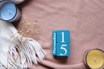 November 15th, Cube wooden calendar showing date on 15 November, Wooden calendar with date and dry flowers on pink knitted sweater.