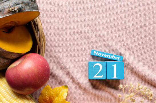 November 21st, Cube wooden calendar showing date on 21 November, Table decorated with Pumpkins ,Corn and Apple.