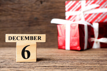 December 6th, Cube wooden calendar showing date on 6 December with red gift box on wooden table.