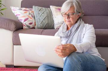 Attractive senior woman at home sitting on the floor using a laptop computer. An elderly retiree...